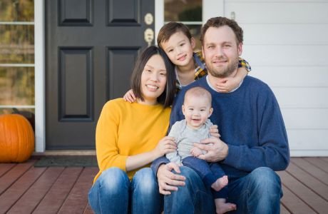 A family of four sits on a porch in front of a black door.